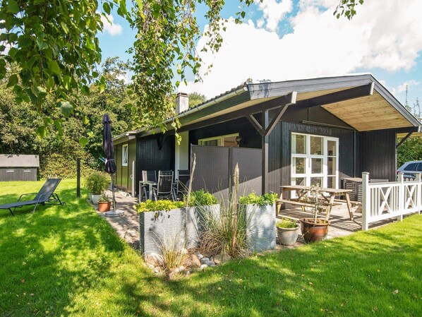Eine Holzhütte mit einer Terrasse, Sitzgelegenheiten im Freien und einem Garten.