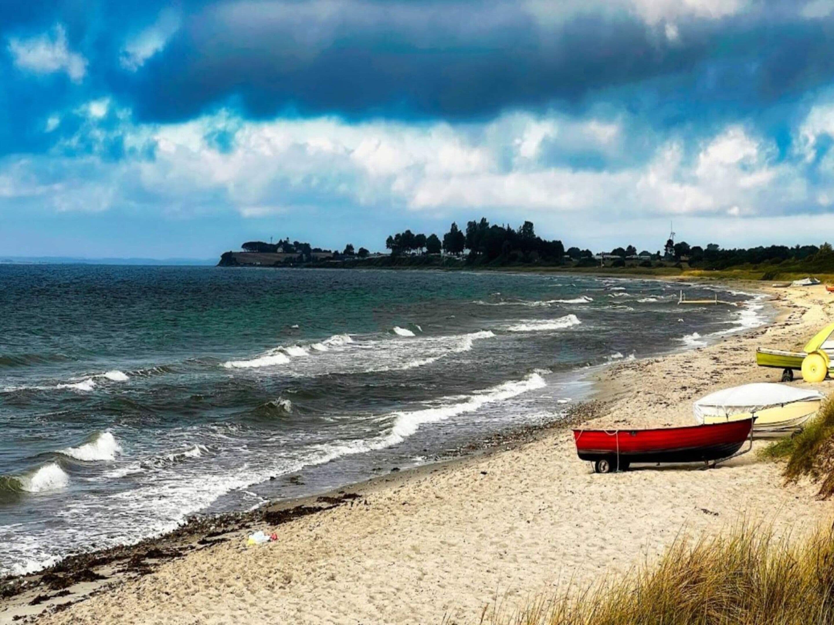 Una playa con un bote rojo, un bote amarillo y un bote blanco sobre la arena.