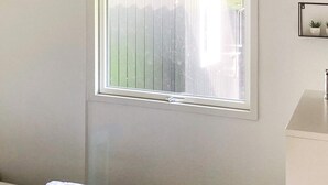 A bedroom with a bed, a window, a wall-mounted shelf with potted plants, and a bathroom with a sink.