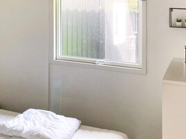 Quarto com cama, janela, prateleira fixada na parede com plantas em vasos e banheiro com pia.