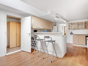 A compact kitchen with wooden cabinets, a small island with stools, and a ceiling-mounted light fixture.