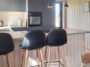 A modern kitchen with wooden accents, a central island, and black bar stools. - 5 Star Holiday Home in Albaek (Aalbaek)