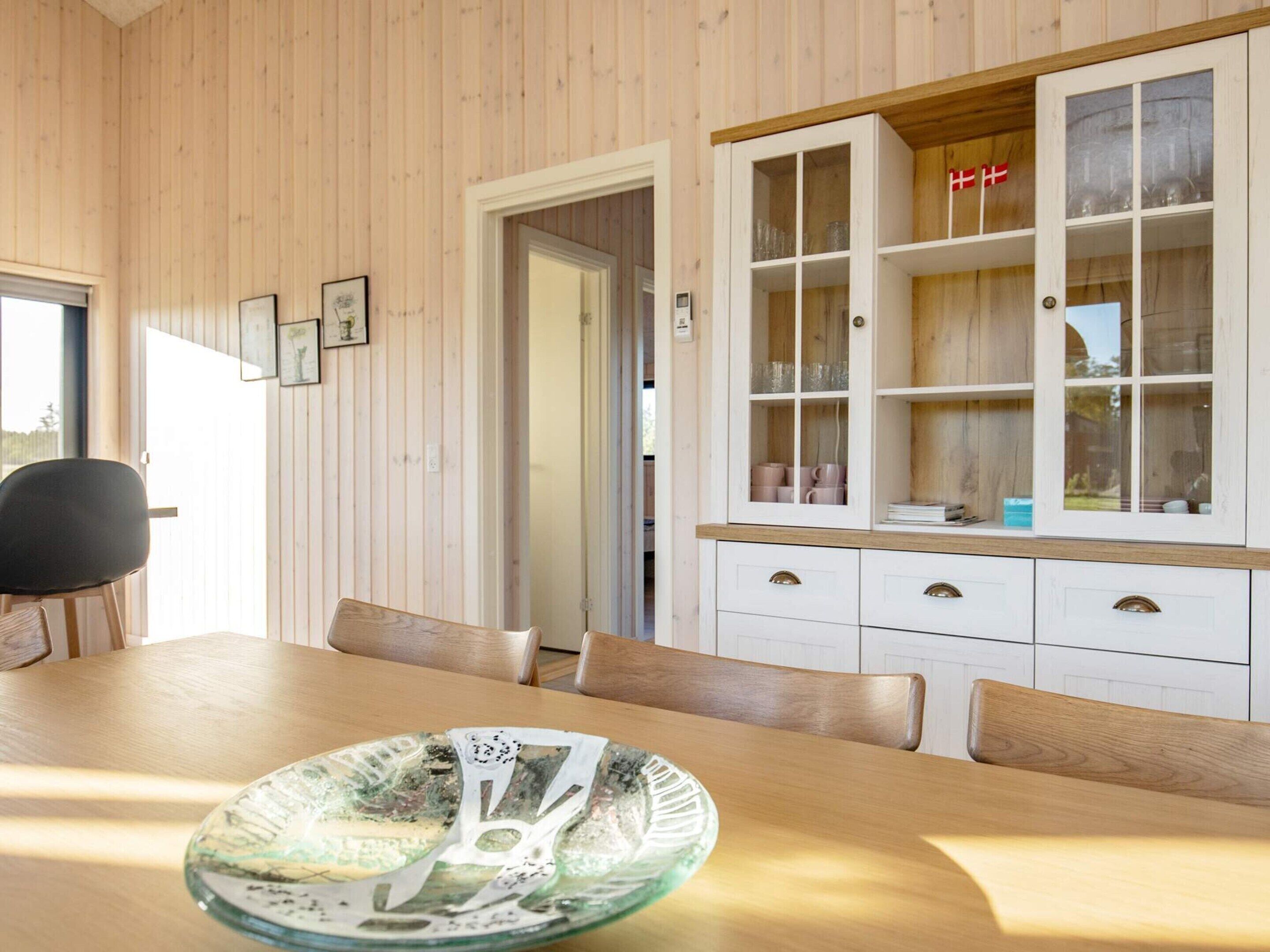 A dining area with a wooden table and chairs, a glass bowl centerpiece, and a white cabinet with glass doors.