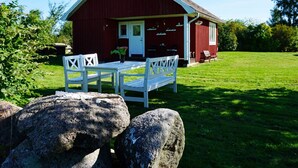 Punainen lato, jossa on valkoinen ovi ja ikkunat, valkoisilla tuoleilla ja pöydällä varustettu kuisti sekä ruohikkoalue.