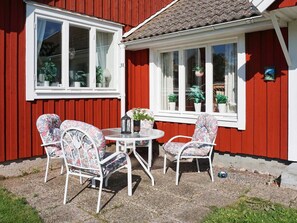A red house with white trim, a small patio with a round table and floral chairs, and potted plants on the windowsill.