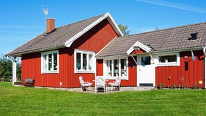Punainen talo, jossa on kalteva katto, savupiippu ja pieni kuisti, jossa on valkoisia tuoleja.