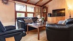 Ett mysigt vardagsrum med ett träpanelat tak, en svart lädersoffa, ett träbord och en tv på väggen.