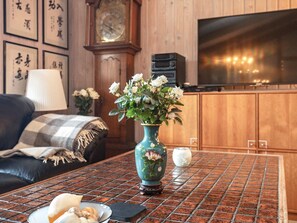 A living room with a sofa, a coffee table with a vase of flowers, a clock, and a television.