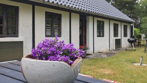 A house with a tiled roof and white walls, a flower pot with purple flowers on a table, and a barbecue grill in the yard. - 6 Person Holiday Home in Laeso (Læsø)