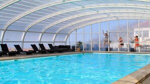 An indoor swimming pool with clear glass walls, lounge chairs, and a pool ladder. - 4 Person Holiday Home in Allinge (Allinge)