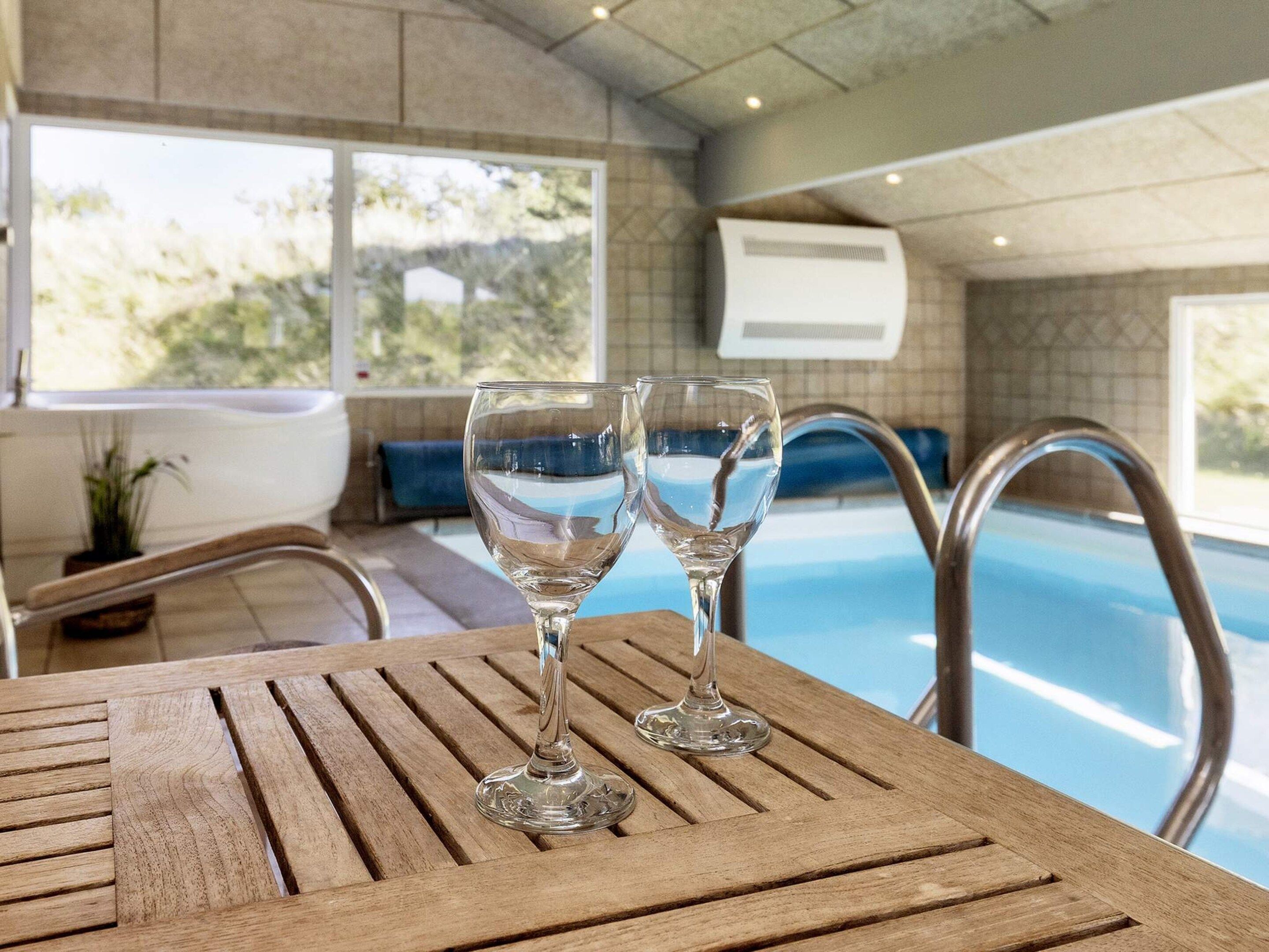 A wooden table with two clear glasses, a pool, and a view of the outdoors.