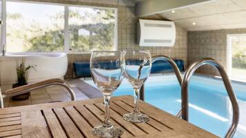A wooden table with two clear glasses, a pool, and a view of the outdoors.