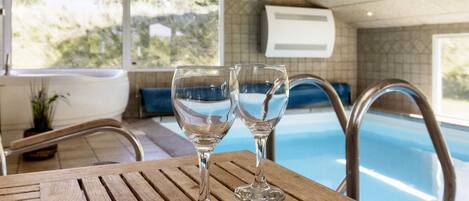 A wooden table with two clear glasses, a pool, and a view of the outdoors.