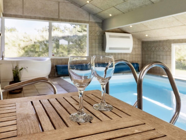 A wooden table with two clear glasses, a pool, and a view of the outdoors.