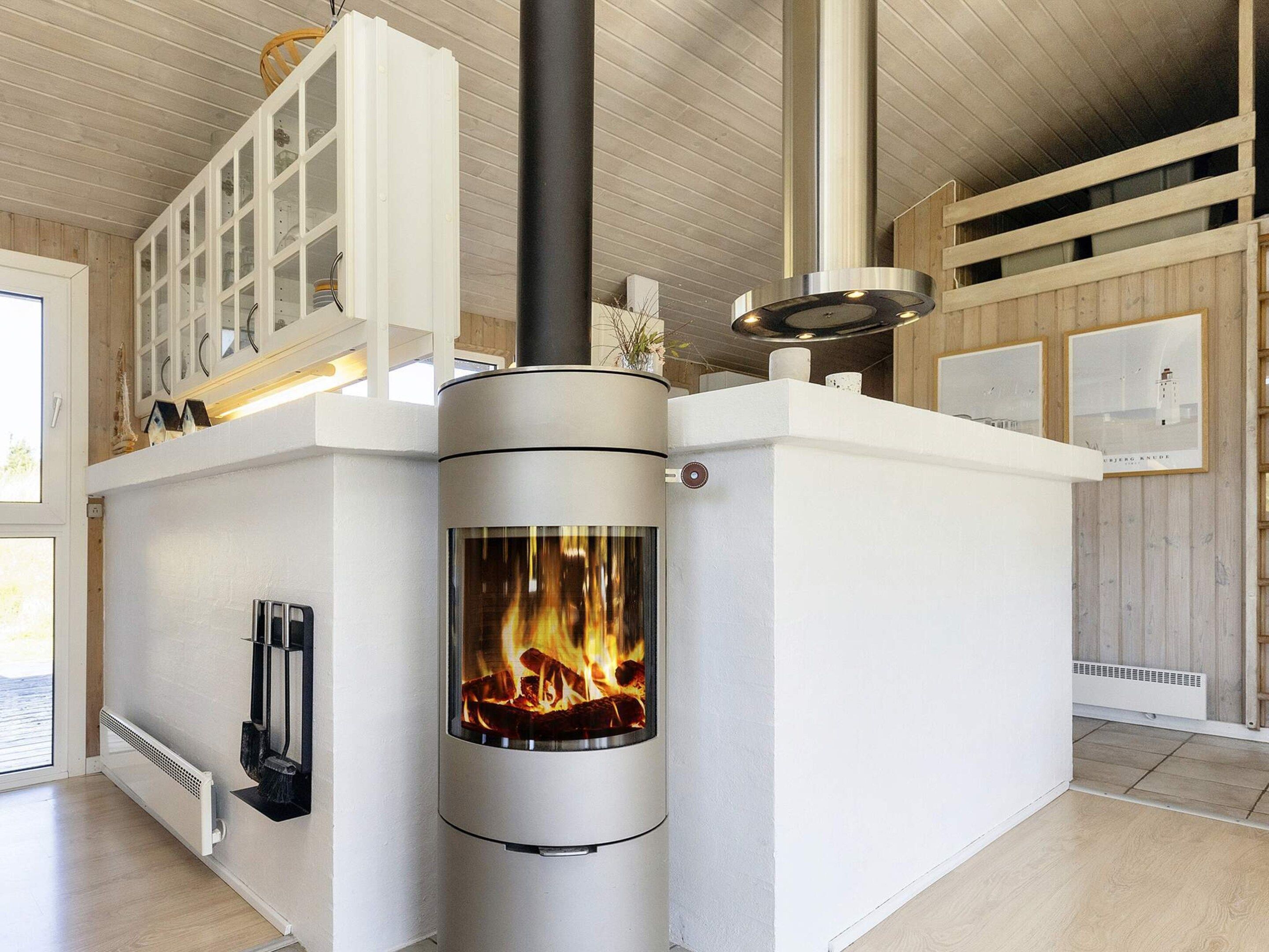 A modern interior with a wood-burning stove, white cabinetry, and a view of the outside.