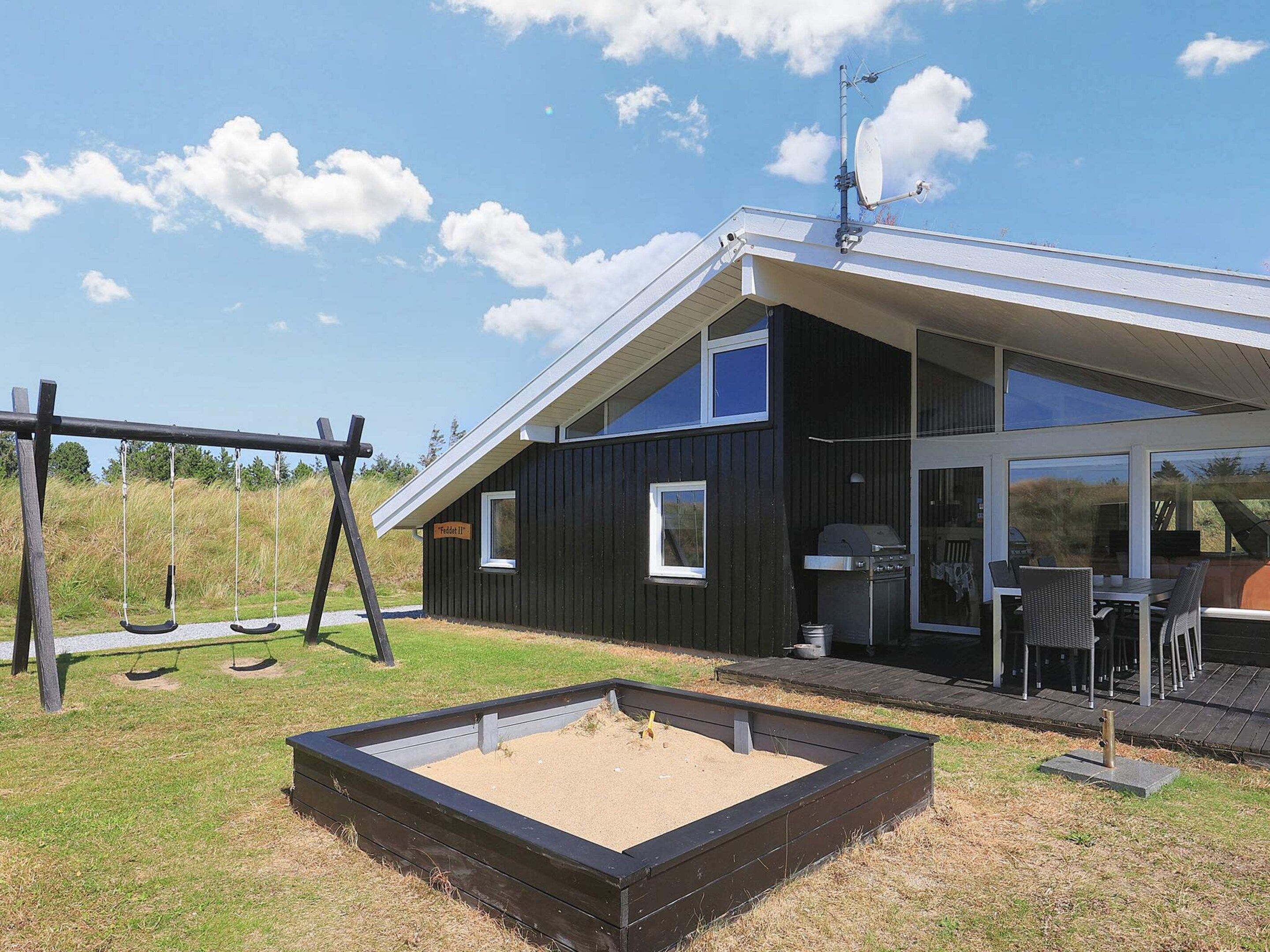 A modern house with a black exterior, a large glass door, and a patio with outdoor furniture.
