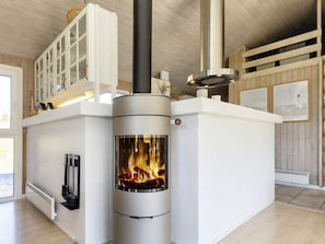 A modern interior with a wood-burning stove, white cabinetry, and a view of the outside. - 14 Person Holiday Home in Blokhus (Blokhus)