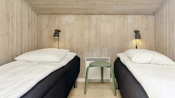 A small, cozy room with two single beds, a small table, and two wall-mounted lamps.