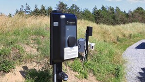 A black outdoor device labeled 'Clever' with a dial, a small box, and a sensor on a post in a grassy area.
