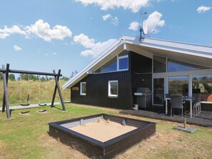 A modern house with a black exterior, large windows, and a patio area with outdoor furniture. - 14 Person Holiday Home in Blokhus (Blokhus)