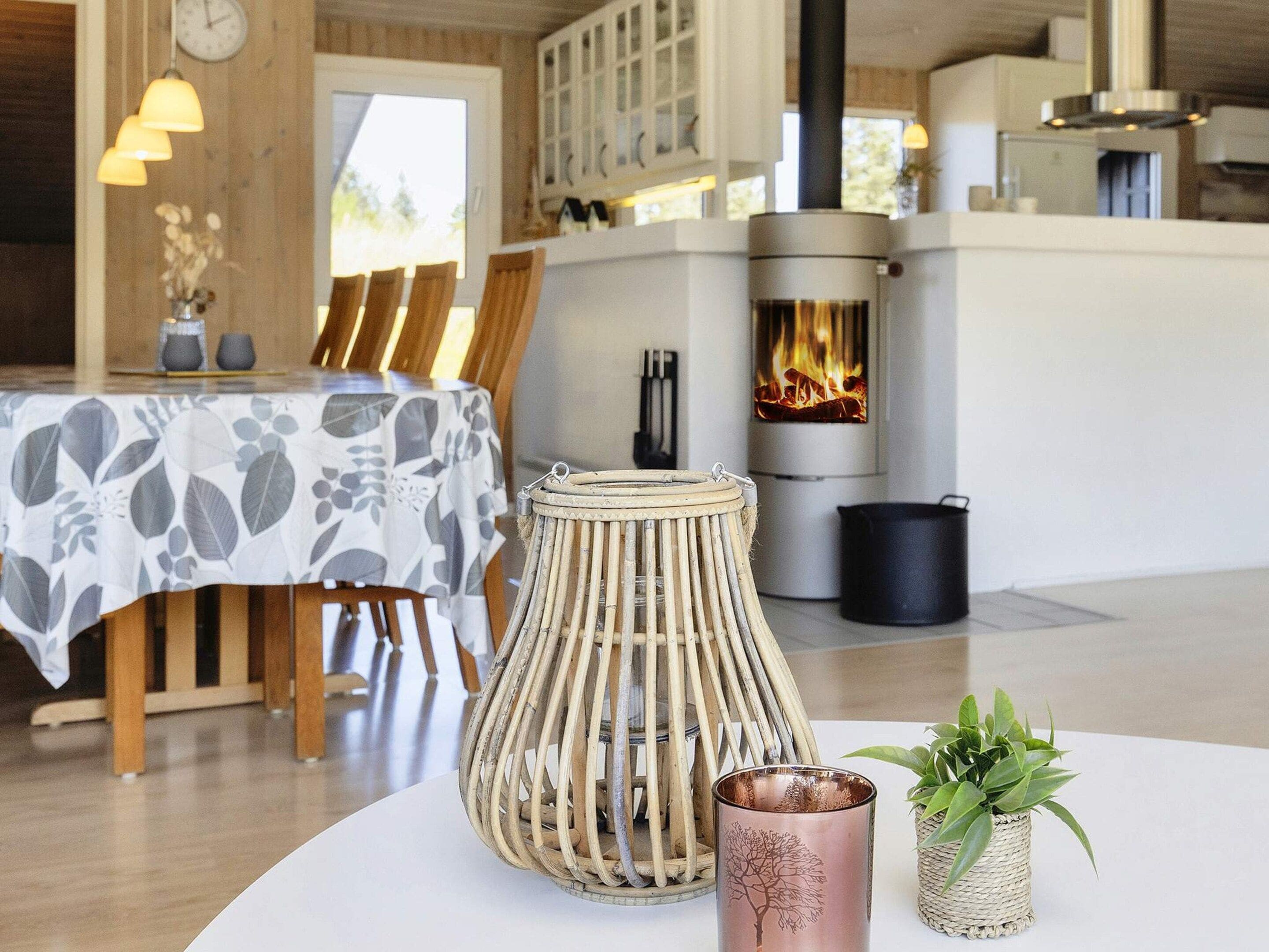 Ein gemütliches Zimmer mit einem runden Tisch, Stühlen, einem gewebten Hocker, einem Kupferkerzenhalter und einer Topfpflanze.