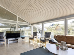 A modern living room with a large TV, comfortable seating, and large windows offering a view of the outdoors. - 14 Person Holiday Home in Blokhus (Blokhus)