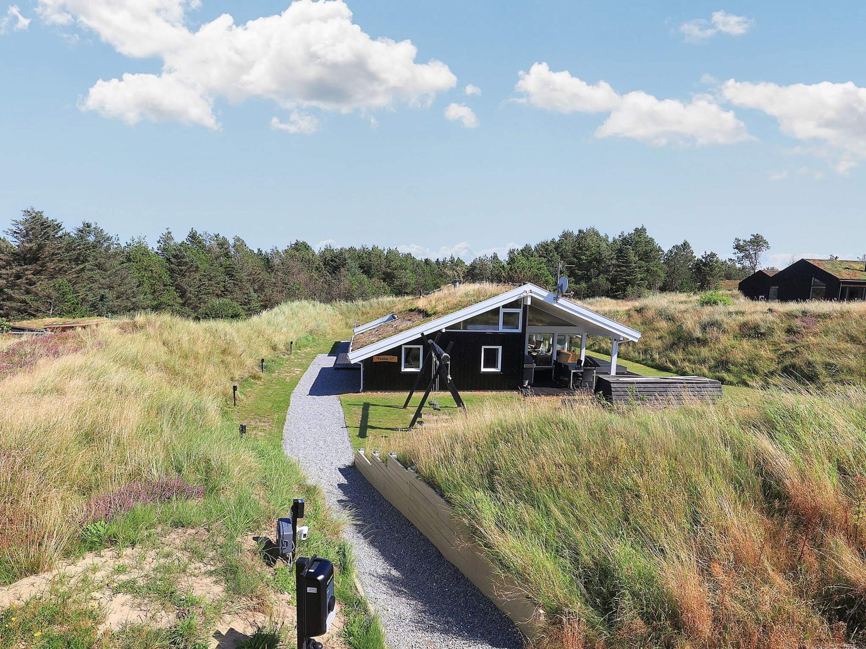 A modern house with a sloped roof, a covered porch, and a gravel path leading to it.