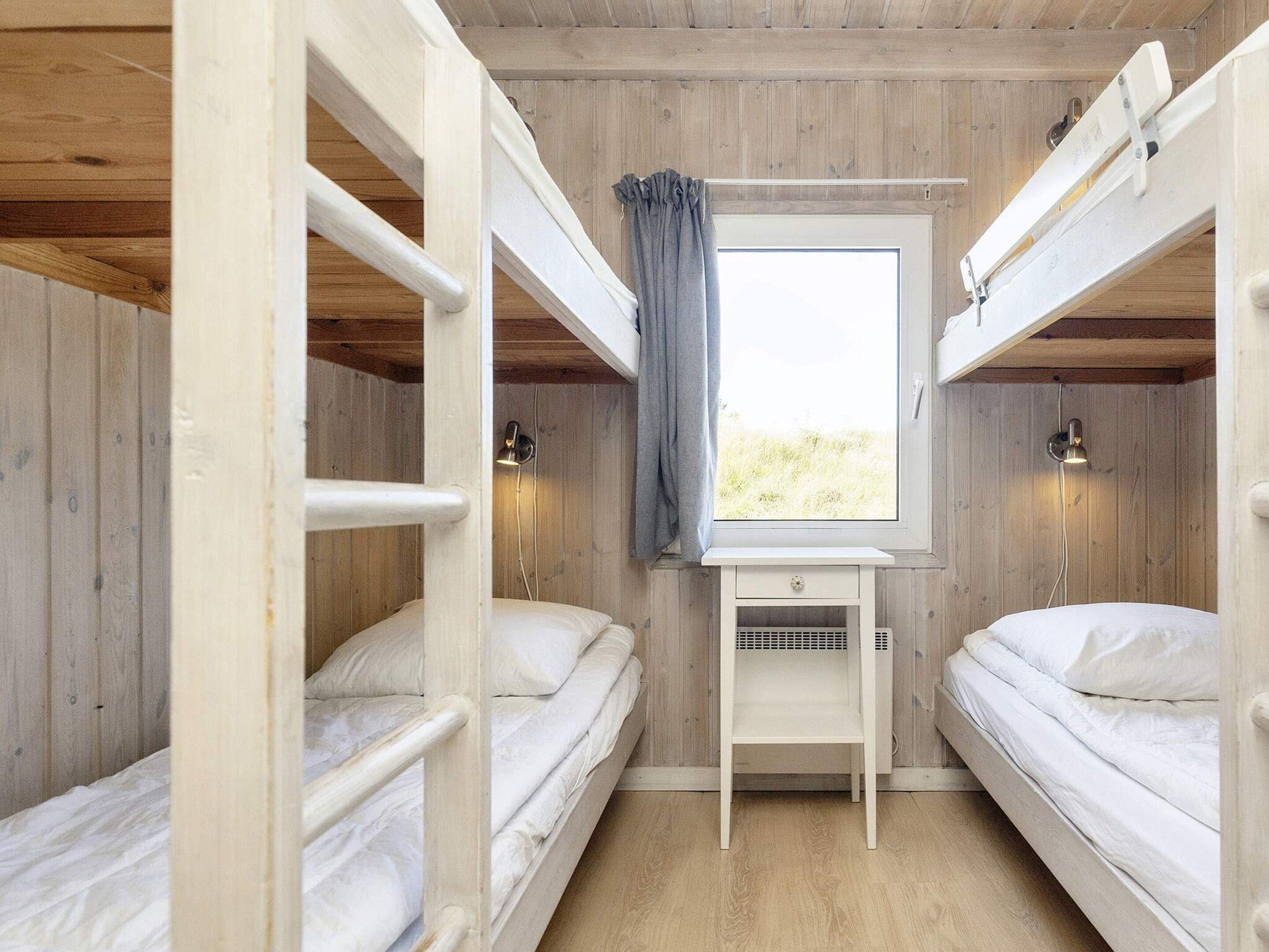 A compact room with bunk beds, a small desk, and a window with curtains.