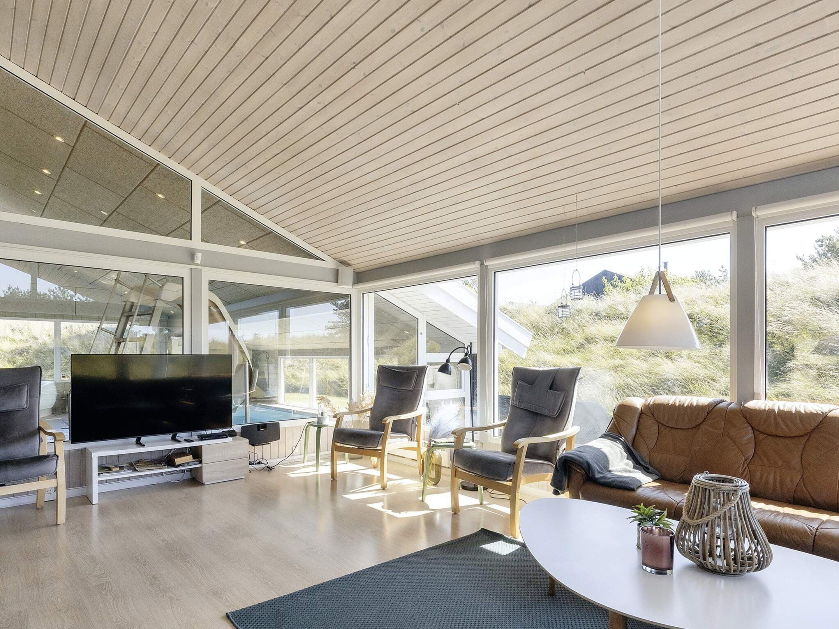 Ein modernes Wohnzimmer mit Fernseher, Sitzgelegenheiten und Blick ins Freie.