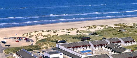 An aerial view of a coastal hotel with multiple buildings, a swimming pool, and a beach in the background.