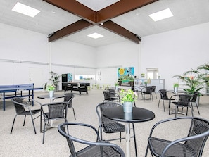 Un grand espace intérieur aménagé avec des tables et des chaises, un billard et des plantes en pot.