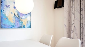 Un comedor moderno con una mesa blanca, un cuenco de aperitivos, un cuadro abstracto grande y un televisor en la pared.