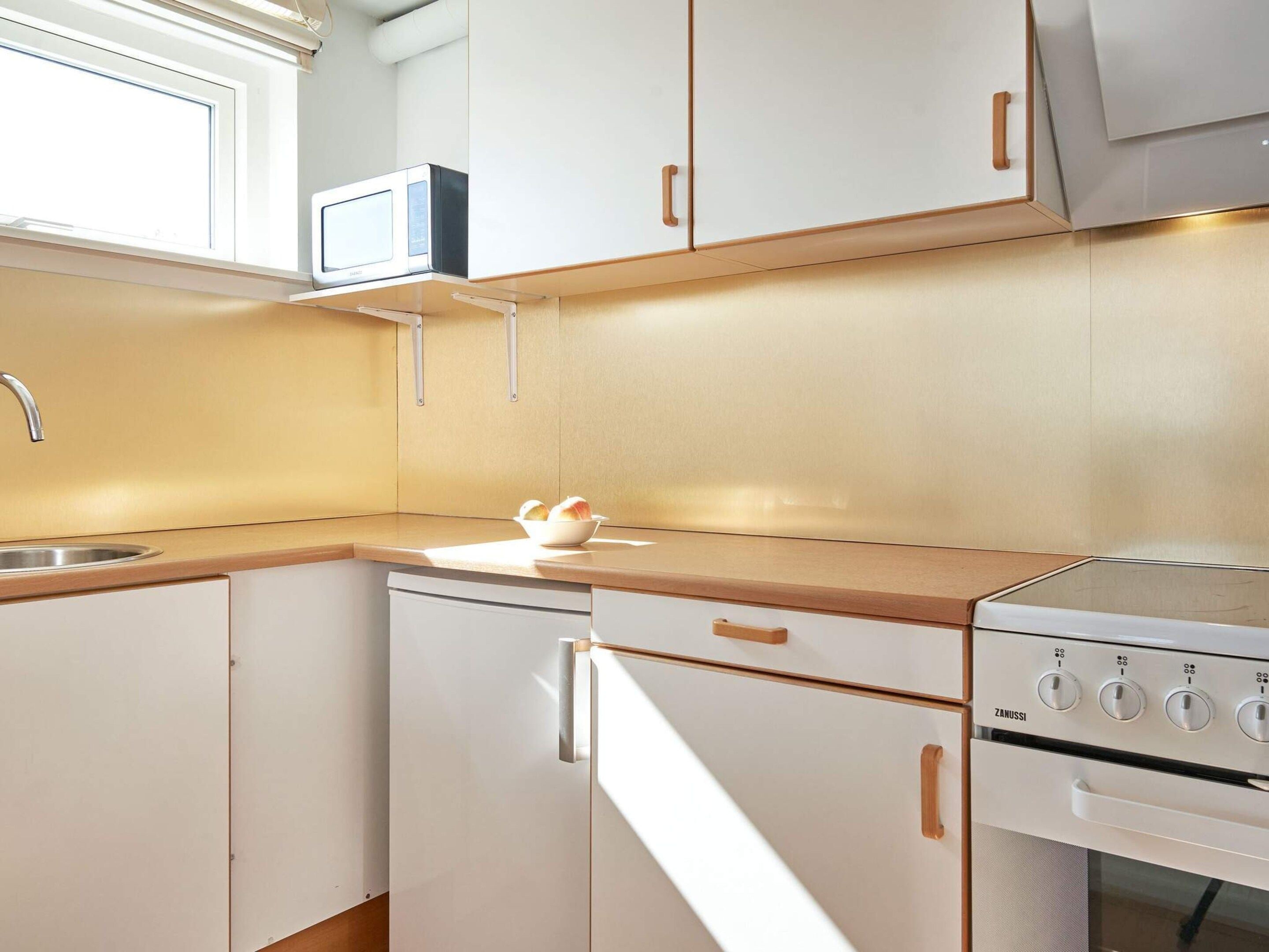 A modern kitchen with white cabinets, a stainless steel sink, a microwave, and a Zanussi oven.