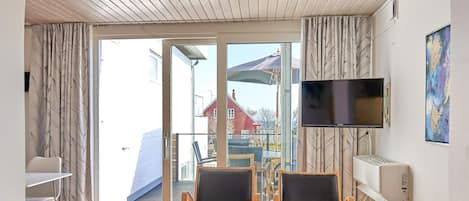 A room with a wooden ceiling, a TV mounted on the wall, and a view of the outside.