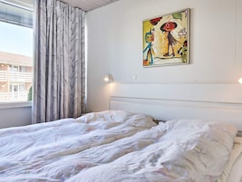 Et soveværelse med seng, gardiner, en lampe på væggen og et maleri.
