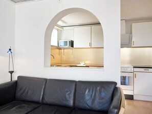 A modern living room with a black leather sofa, a kitchen visible through an arched window, and a blue floor lamp. - 4 Star Holiday Home in Allinge (Allinge)