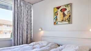 Un dormitorio con cama, cortinas, una lámpara fijada a la pared y un cuadro.