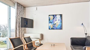 Una sala de estar moderna con una mesa de madera, dos sillas, un sofá, un televisor de pantalla plana y un cuadro en la pared.
