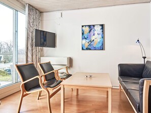 A modern living room with a wooden table, two chairs, a sofa, a flat-screen TV, and a painting on the wall. - 4 Star Holiday Home in Allinge (Allinge)