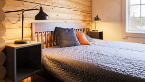 A cozy bedroom with a wooden headboard, a quilted bedspread, two bedside lamps, and a window with a view of greenery. - 10 Person Holiday Home in Vaeggerlose-by Traum (Vaeggerlose)