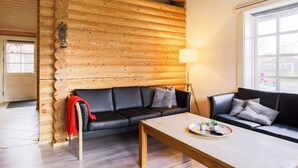A cozy living room with a wooden log wall, two black leather sofas, a wooden coffee table, and a large window providing natural light. - 10 Person Holiday Home in Vaeggerlose-by Traum (Vaeggerlose)