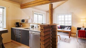 A modern kitchen with a wooden log feature, a dining area with a red chair, and a living room with a sofa. - 10 Person Holiday Home in Vaeggerlose-by Traum (Vaeggerlose)