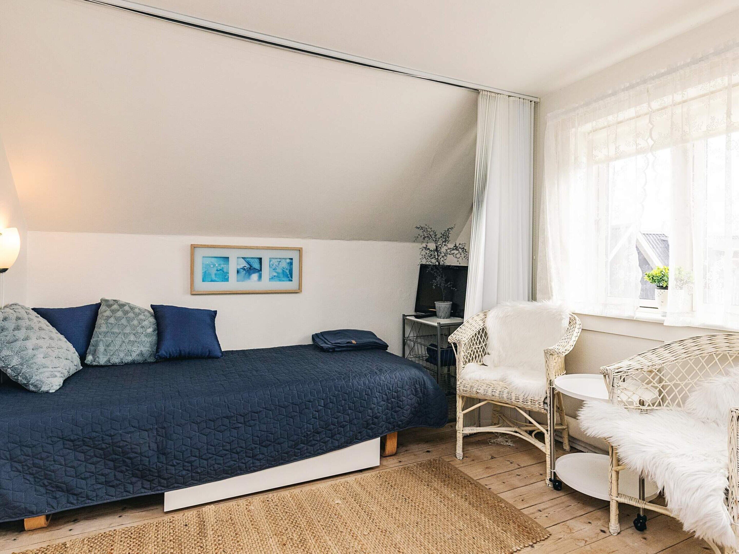 Un dormitorio con una cama, una silla, una mesita y una ventana con cortinas.
