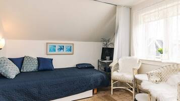 Un dormitorio con una cama, una silla, una mesita y una ventana con cortinas.