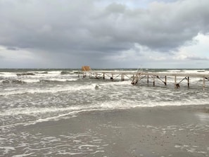 A beach with a wooden pier extending into the ocean, waves crashing onto the shore, and a cloudy sky. - 8 Person Holiday Home in Bagenkop (Sydlangeland)
