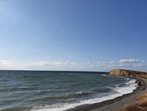 A coastal landscape with a pebbly beach, a cliff, and the ocean.