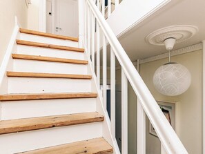 Un escalier avec des marches en bois et des rampes blanches, un luminaire blanc au plafond et une porte au fond.
