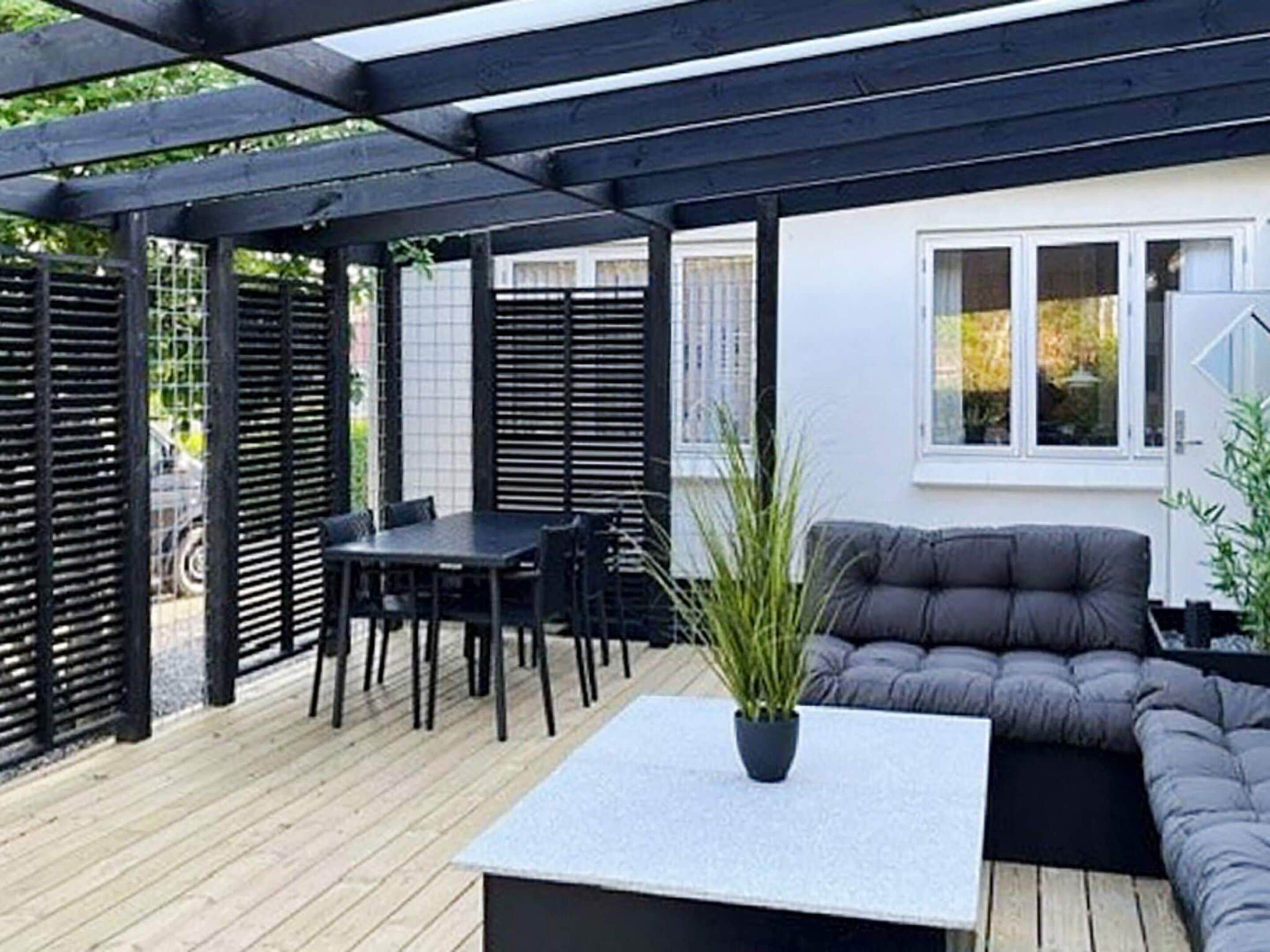 Un espace extérieur abrité, aménagé avec une table et des chaises, un banc rembourré et un pot de fleurs.