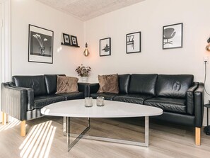 Una sala de estar moderna con un sofá de cuero negro, una mesa de centro blanca y obras de arte enmarcadas en las paredes.