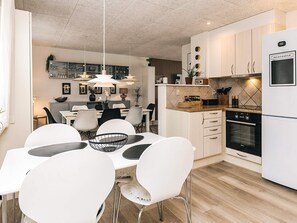 A modern kitchen with white cabinetry, a built-in oven, and a dining area with white chairs and a table. - 8 Person Holiday Home in Bagenkop (Sydlangeland)